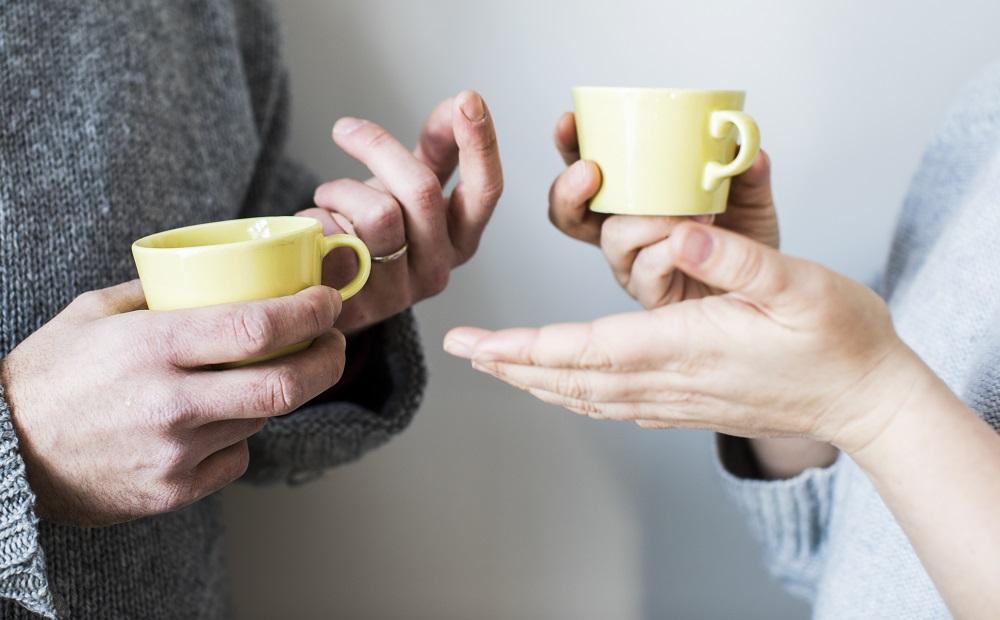Händerna av två personer som diskuterar. De har gula kaffekoppar i sina händer.