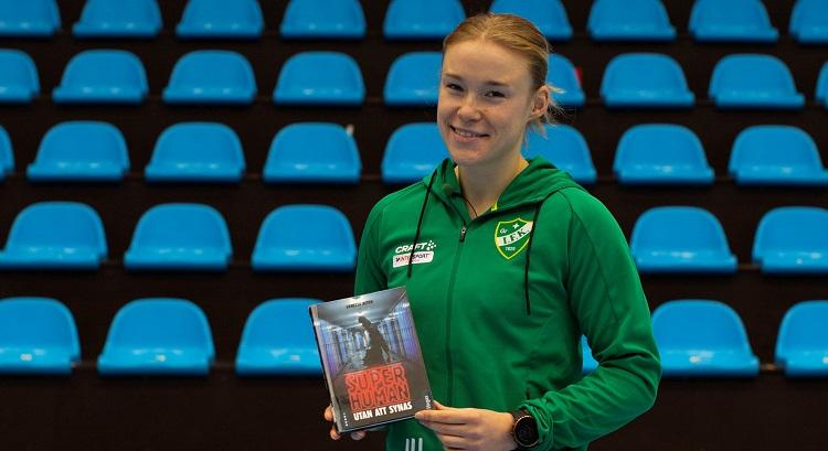 Handbollsspelaren Johanna Hilli i sportkläder framför en läktare och med en bok i handen.